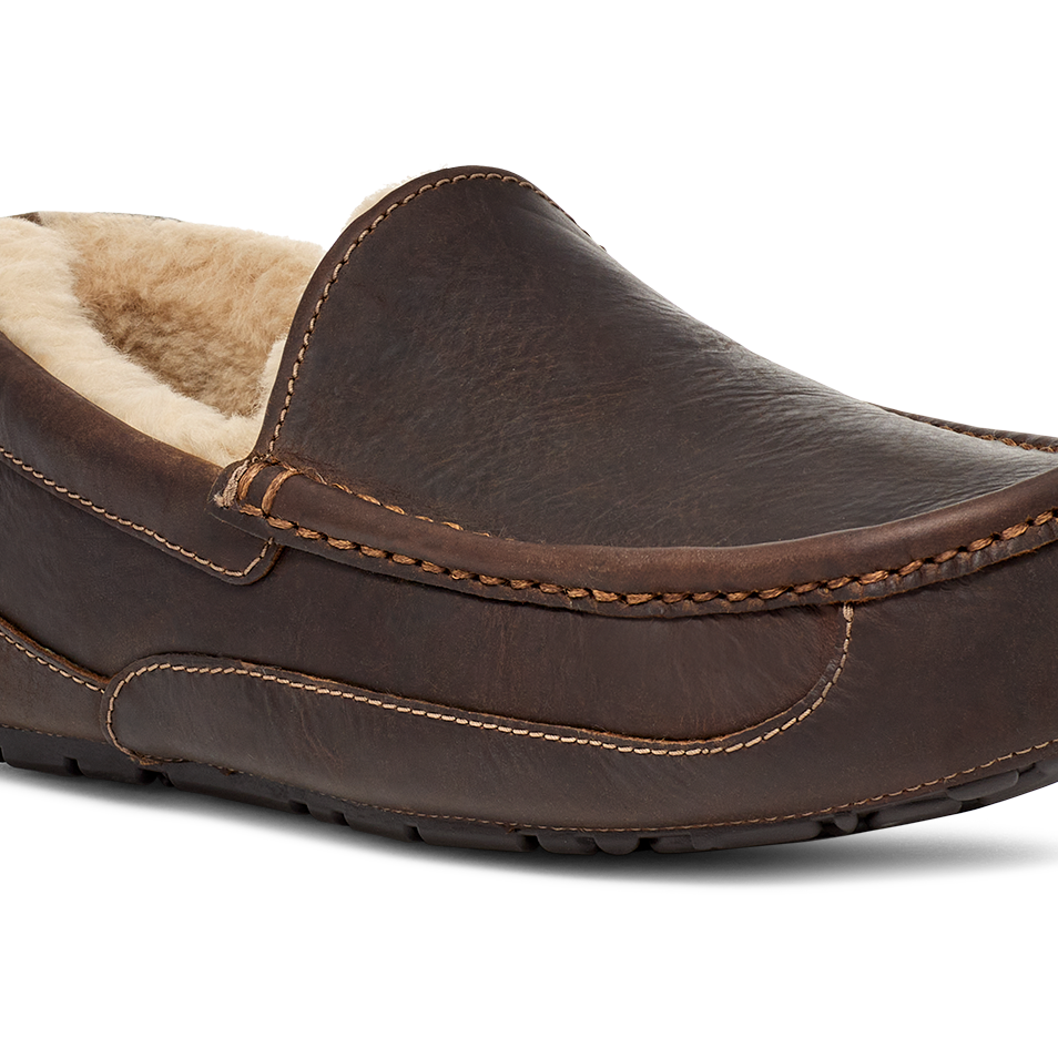 A single dark brown leather slip-on moccasin-style shoe with a light beige sherpa lining, shown from a three-quarters angle on a white background.