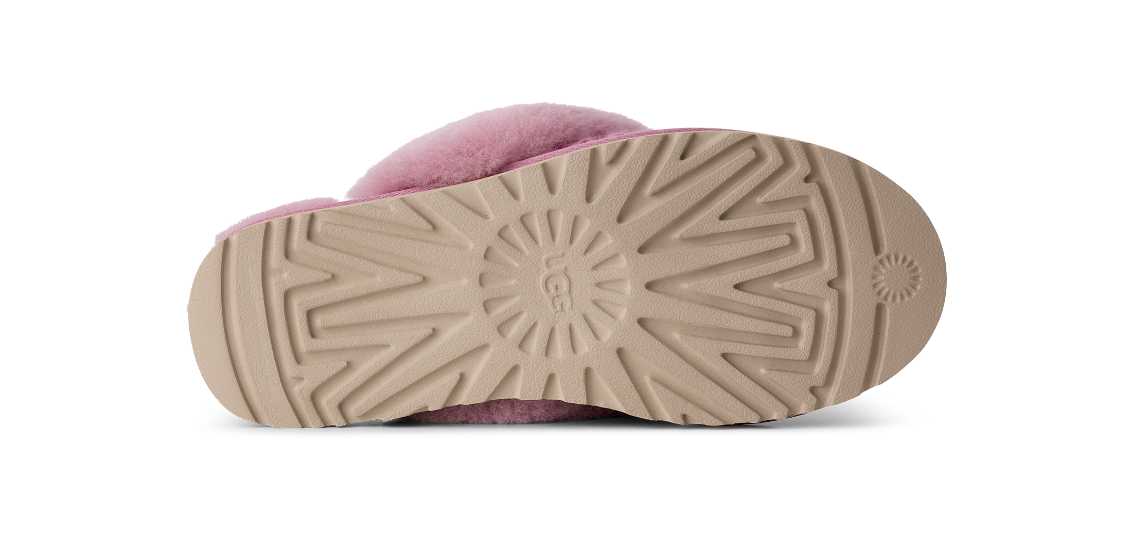 The bottom sole of a pink fuzzy slipper, showing a beige treaded rubber outsole with a circular UGG logo embossed in the center, photographed on a white background.