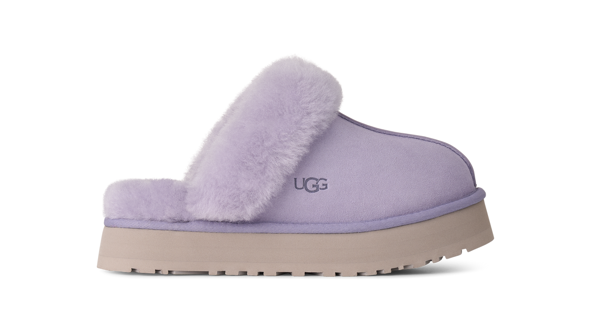 A single UGG slip-on mule slipper in light lavender purple, featuring a soft fuzzy shearling collar and a thick beige platform sole, shown against a plain white background.