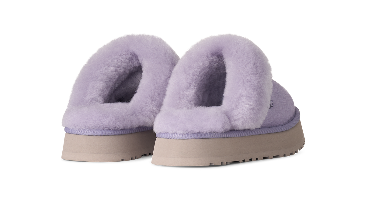 A pair of UGG platform slip-on slippers in light purple lavender, featuring soft fuzzy shearling lining and beige soles, shown against a plain white background.