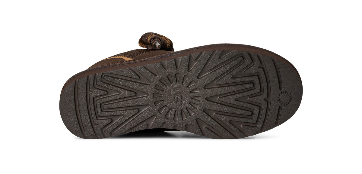 A close-up view of the textured brown outsole of a shoe, showing a circular center tread pattern and a small circular logo on the heel, set against a plain white background.