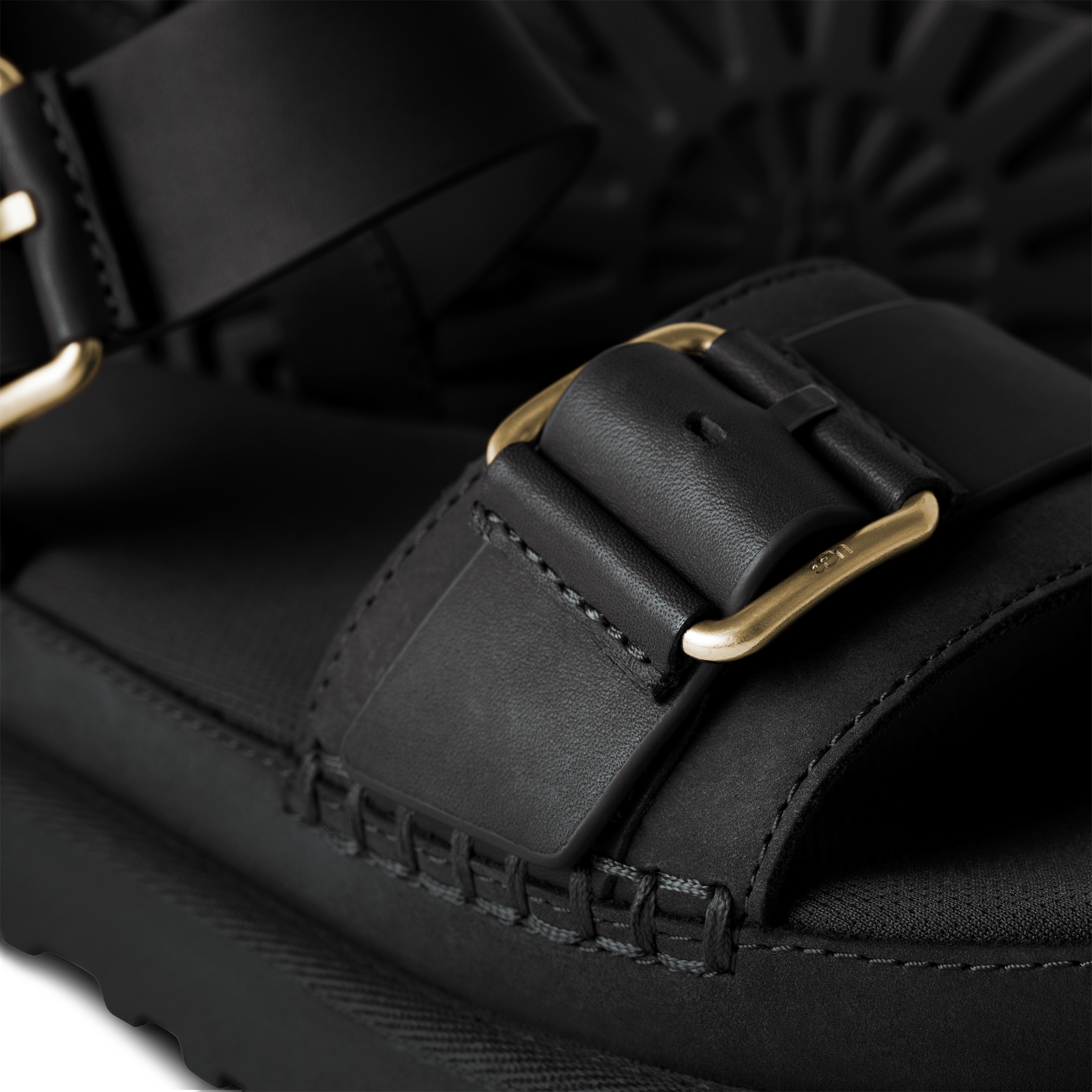 Close-up of a black sandal with gold buckle on a dark background