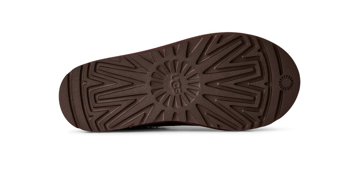 A close-up, top-down view of a dark brown shoe sole, showing its textured tread pattern and a small circular logo near the heel, set against a plain white background.