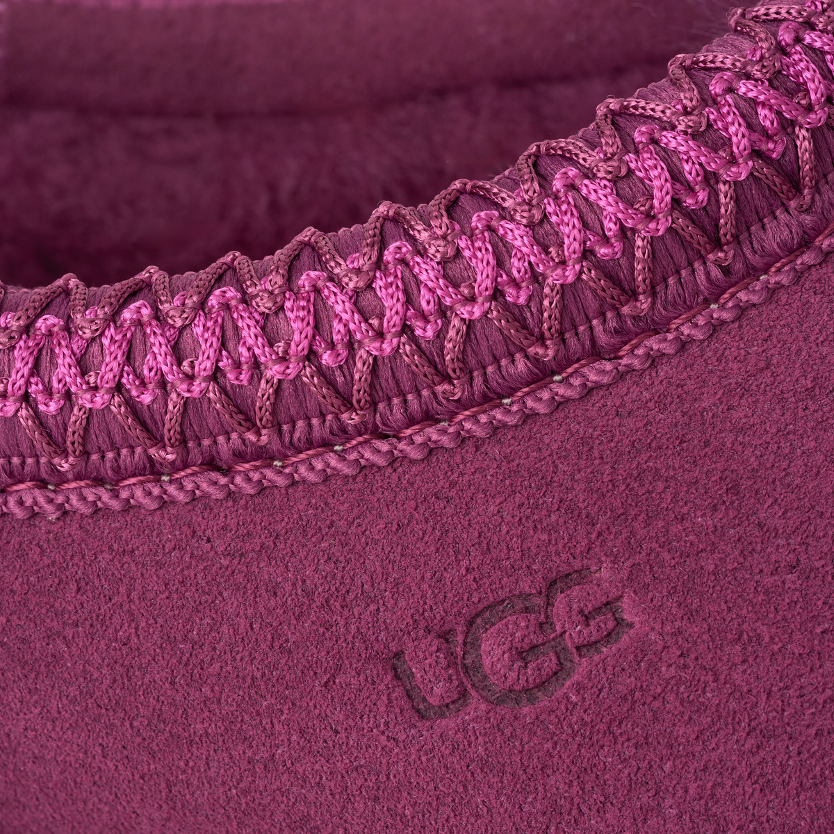 Close-up of a plush mauve-pink UGG slipper interior showing the fuzzy fabric texture, a braided elastic trim, and an embossed UGG logo.