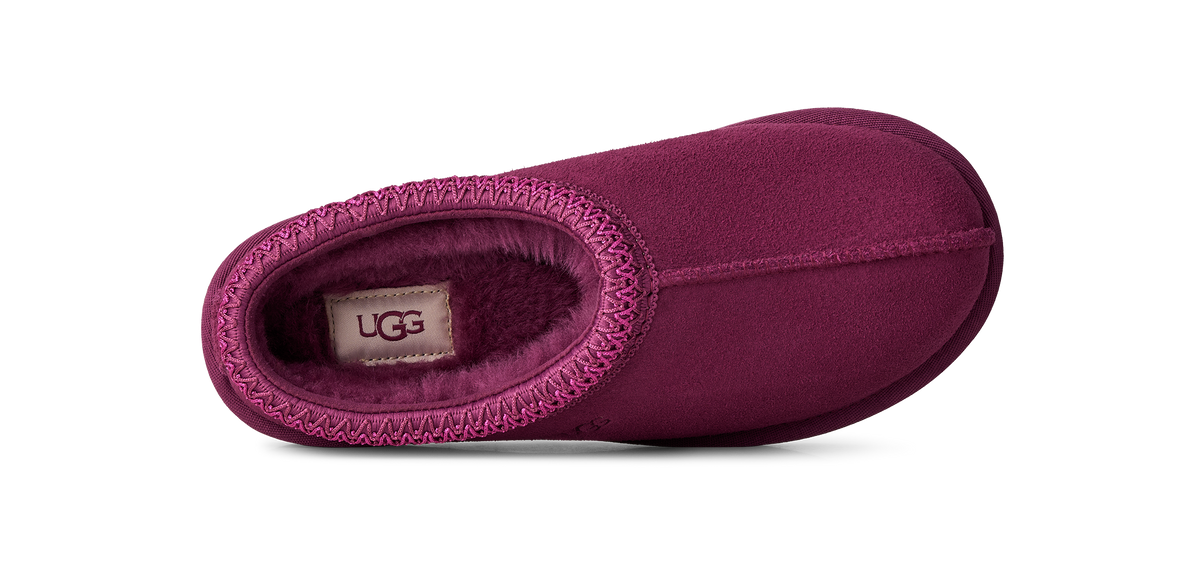 A single UGG slipper in a deep magenta-purple suede-like finish with a matching fuzzy interior and a visible UGG label inside, shown from a top-down angle on a white background.