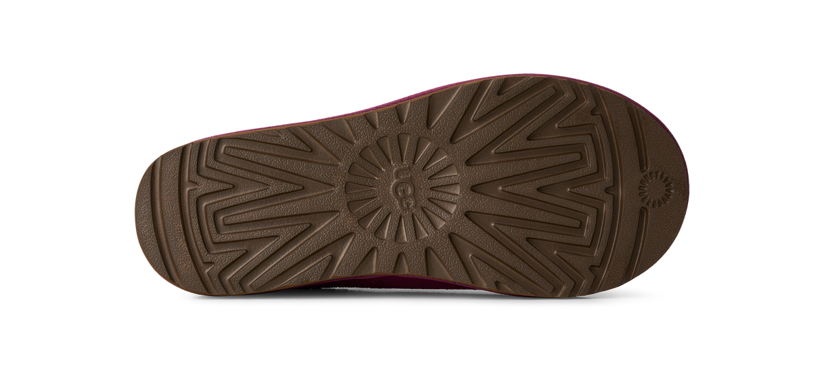 The bottom sole of a shoe, featuring a dark brown textured tread pattern with a circular logo in the center and a small sunburst mark on the heel, shown against a plain white background.