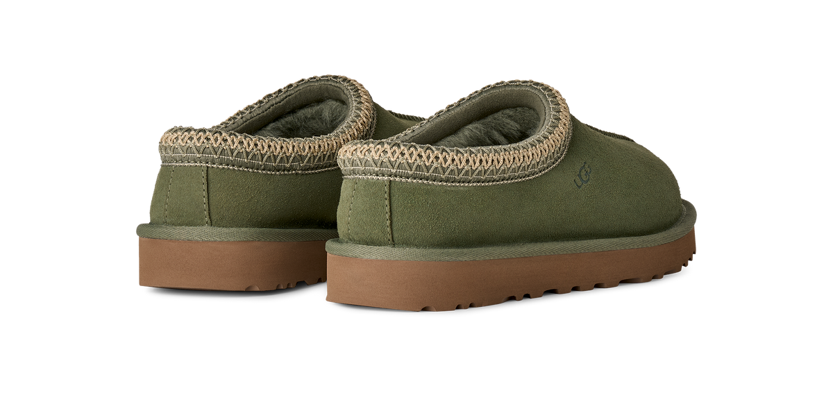 A pair of UGG slip-on slippers in olive green suede with a tan braided trim and brown rubber soles, shown from a three-quarters angle on a white background.