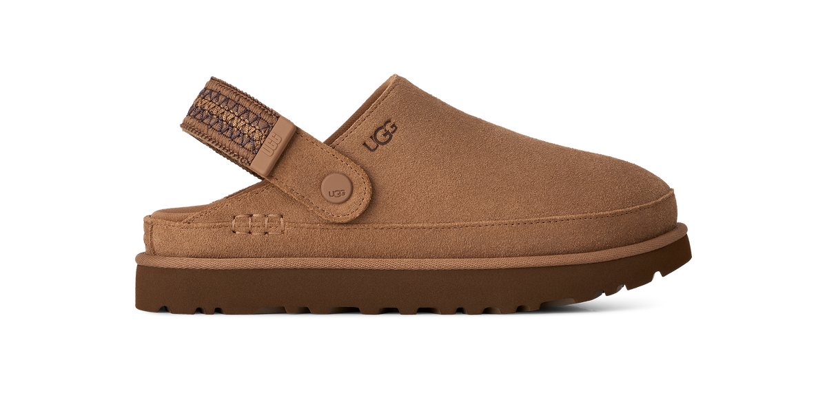A single UGG slip-on clog shoe in a warm tan-brown suede-like material, shown from the side against a solid white background. The shoe features a patterned brown strap with a metal buckle and a thick brown sole.