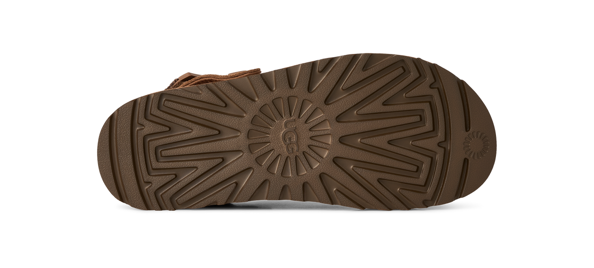 The brown rubber outsole of a boot, showing a detailed tread pattern and a small embossed logo on the heel, photographed against a solid white background.