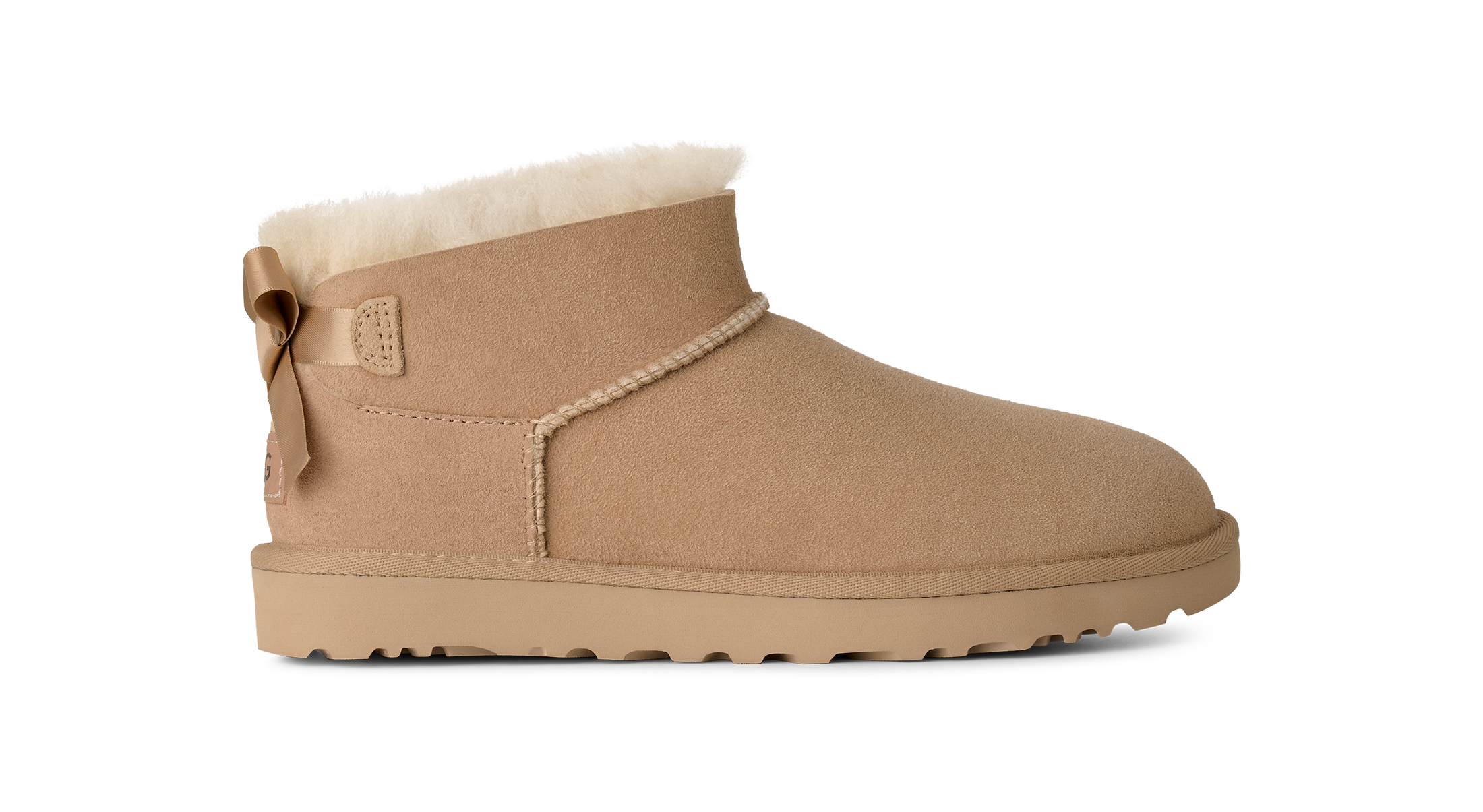 A single beige suede ankle boot with a white shearling lining, a decorative side bow, and a thick lug sole, shown in profile against a white background.