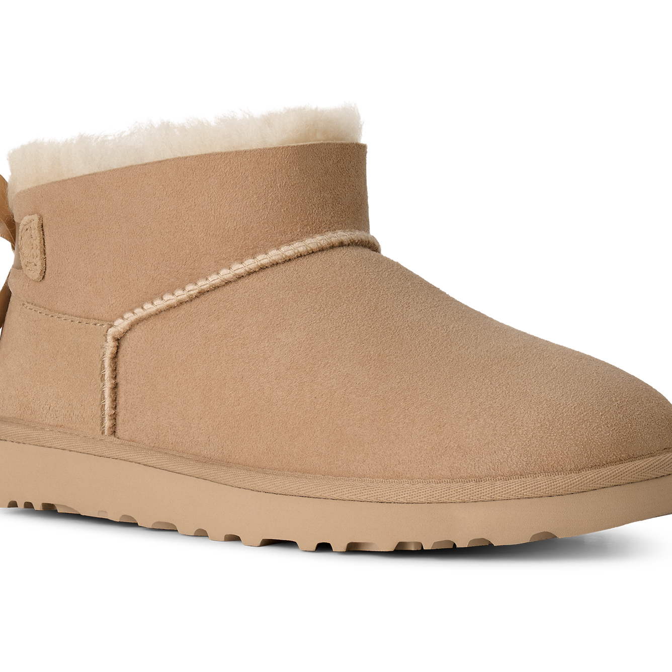 A single tan suede ankle boot with a white shearling lining, a decorative side bow, and a thick lug sole, shown on a plain white background.