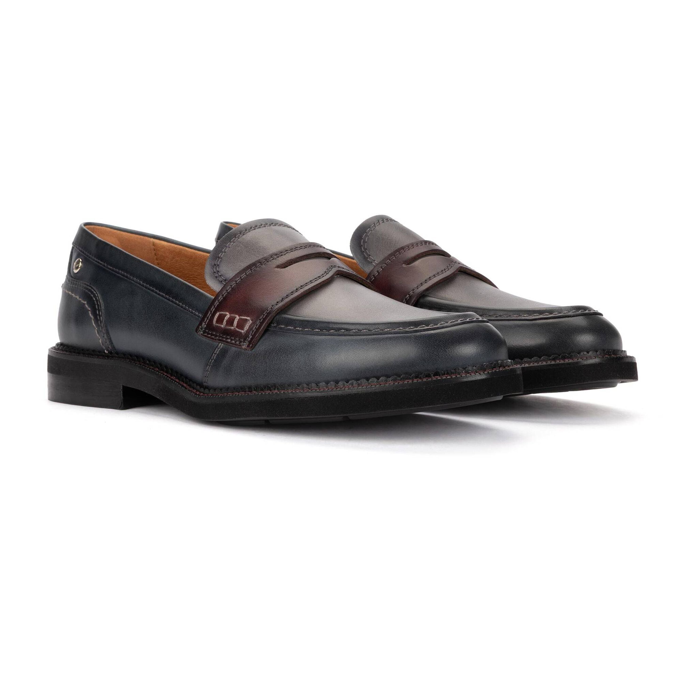 A pair of dark navy blue leather penny loafers with brown leather straps and a tan interior lining, displayed on a clean white background.