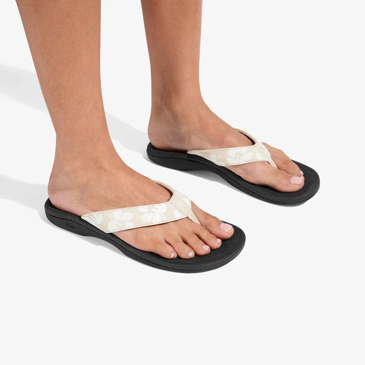 Black sandals with white straps worn by a person on a light gray background