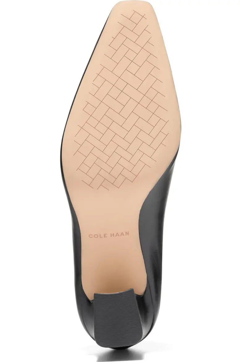 The outsole view of a Cole Haan pointed-toe pump, showing a black leather exterior and a beige rubber footbed with a geometric tread pattern.