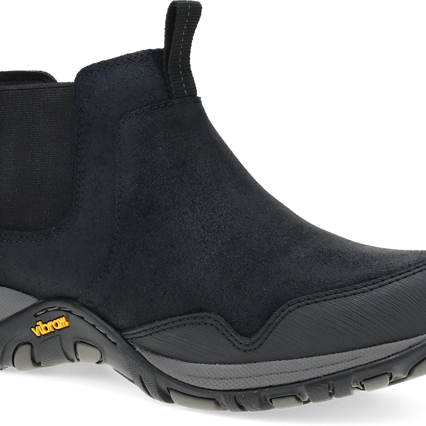 A black Chelsea-style ankle boot with a textured suede-like upper, elastic side gore, and a rugged black sole with a small yellow Vibram logo, shown on a white background.