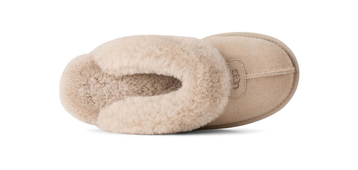 A single UGG slipper in beige suede with a soft cream shearling lining, shown from a side profile view against a solid white background.