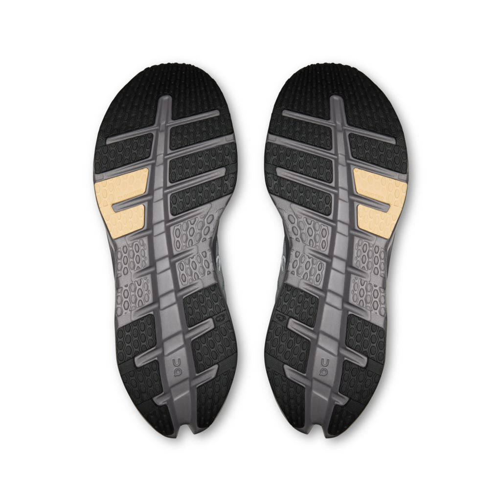 A pair of athletic shoe soles shown from above on a plain white background. The soles are primarily black and dark gray with textured tread patterns and two small tan accents near the heel area.