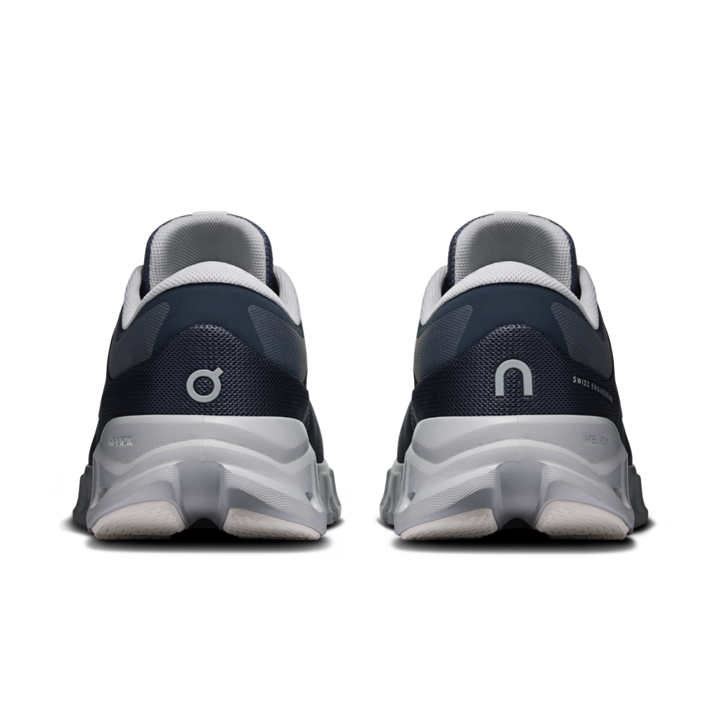 A pair of On running shoes shown from the rear, featuring a navy blue and white design with the brand's logo on the heel counters and a chunky white sole.