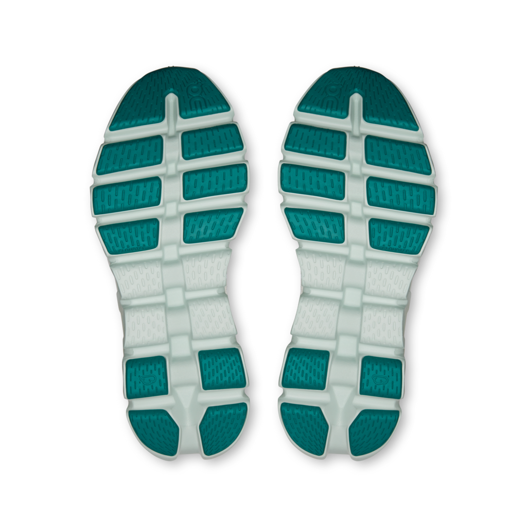 A pair of athletic shoe soles shown from the bottom, featuring a white midsole and teal-green textured outsole blocks, isolated on a white background.