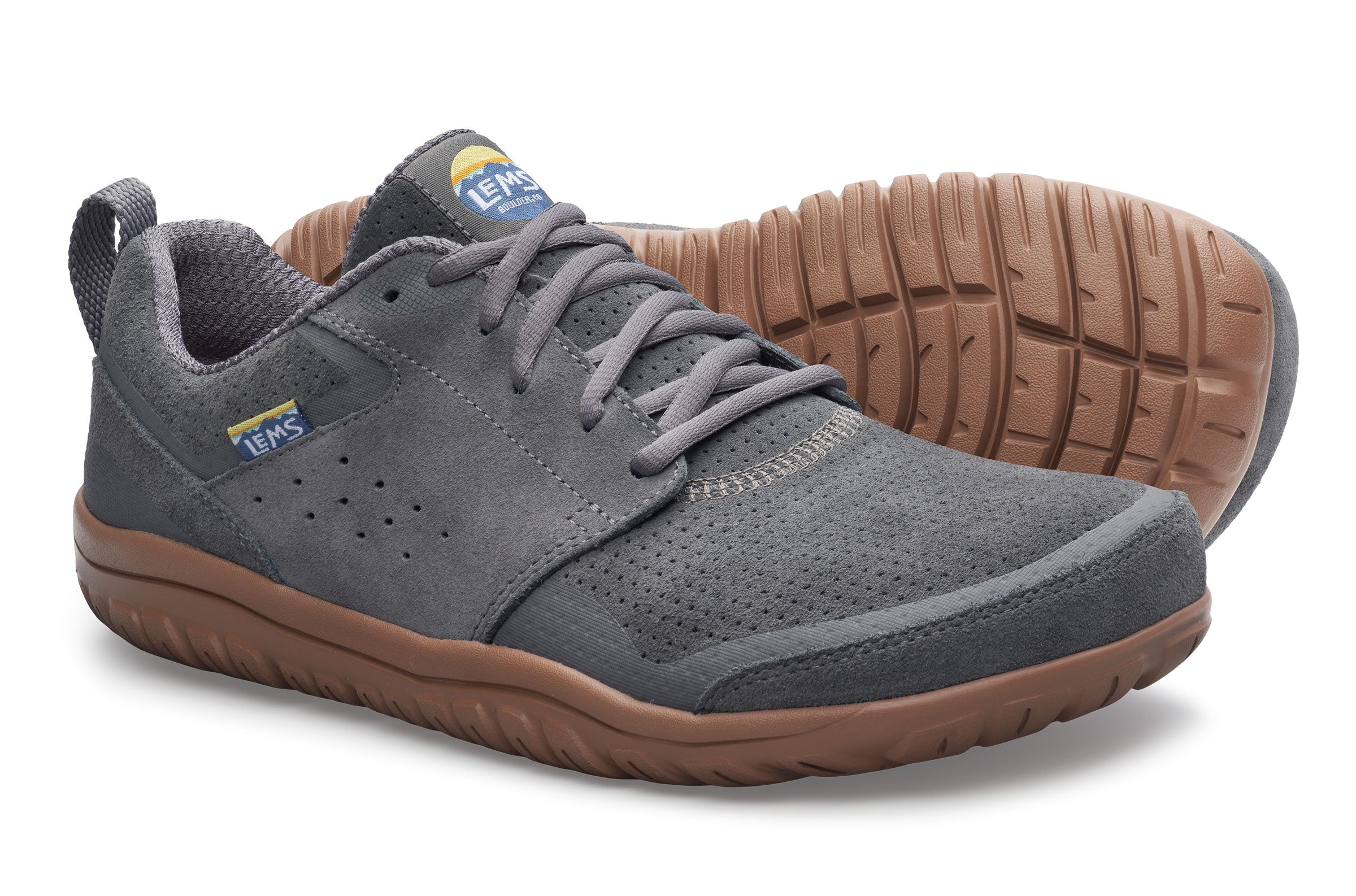 A pair of low-top shoes in dark gray suede and mesh, featuring brown rubber soles and a small blue and yellow logo accent on the side and tongue.