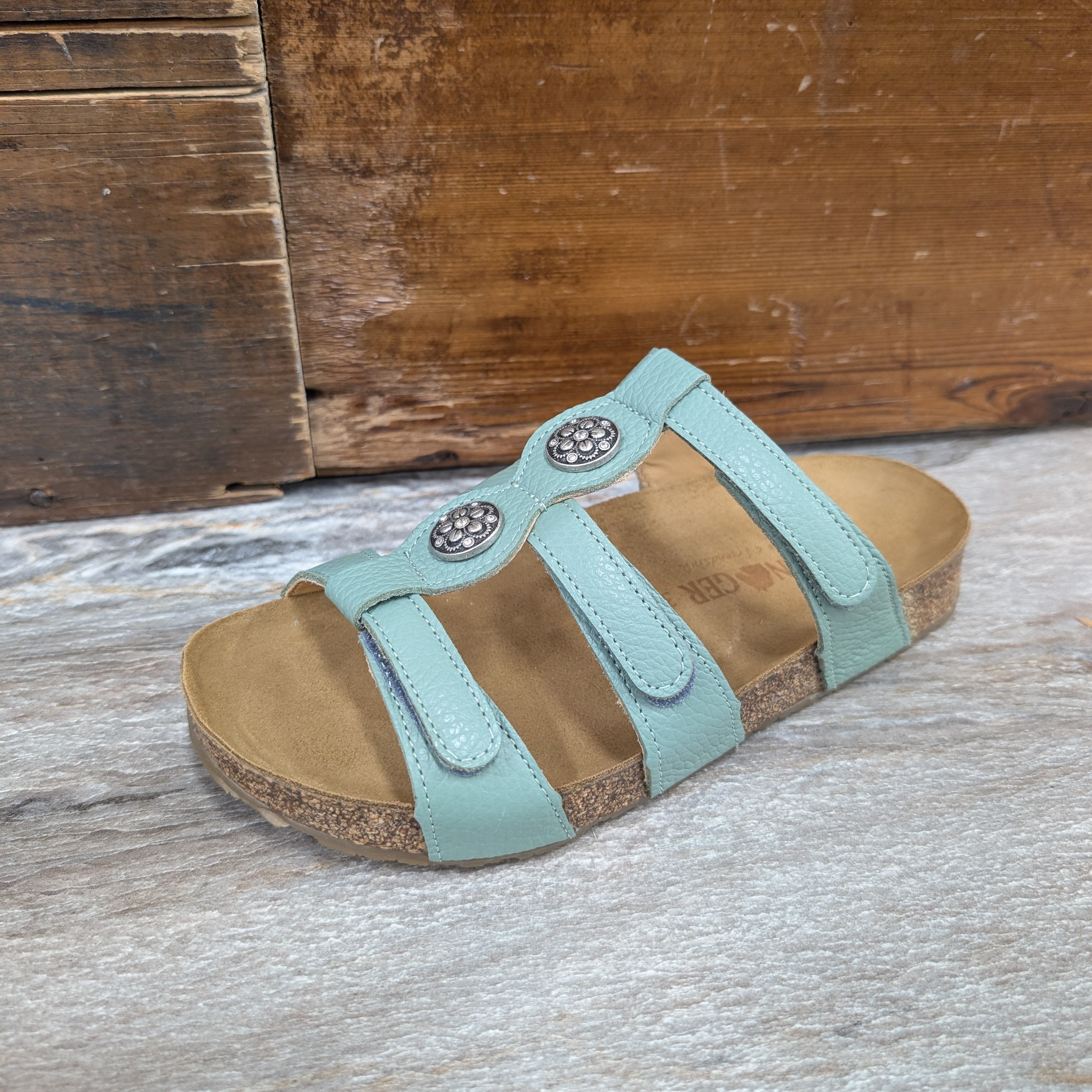 Teal sandal with brown sole on a wooden surface