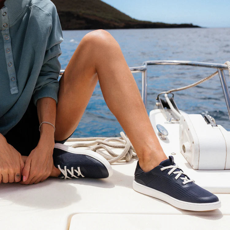 Person wearing navy blue sneakers with white laces on a boat by the water.