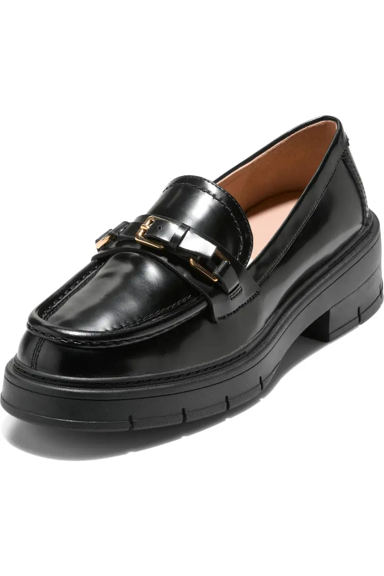 A black leather platform loafer with a chunky sole and a gold-tone decorative strap on the vamp, shown from a three-quarters angle on a white background.