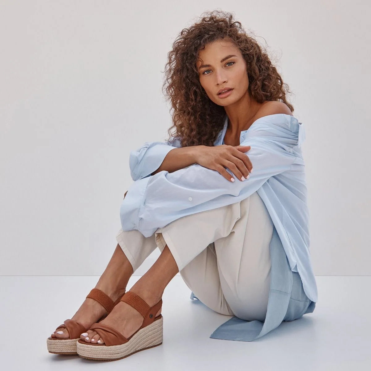 Woman wearing brown sandals with a light blue top and white pants on a white background