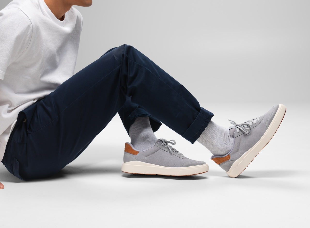 Person wearing gray sneakers with brown accents sitting on a light gray background