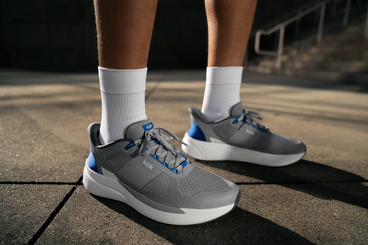 Gray running shoes with blue accents worn by a person on a pavement.