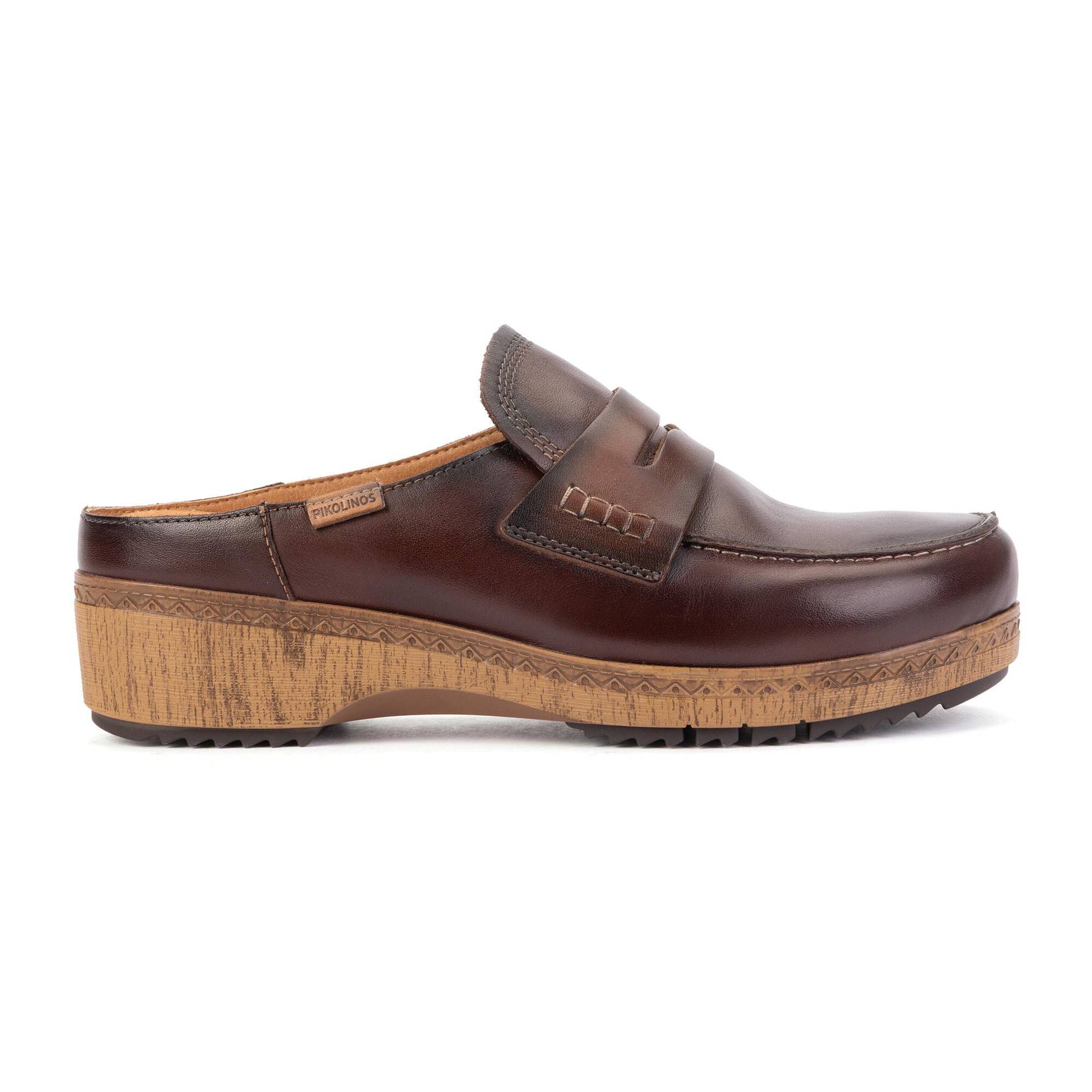 A dark brown leather clog shoe with a thick, textured natural cork wedge heel and sole, shown in a side profile view against a plain white background.