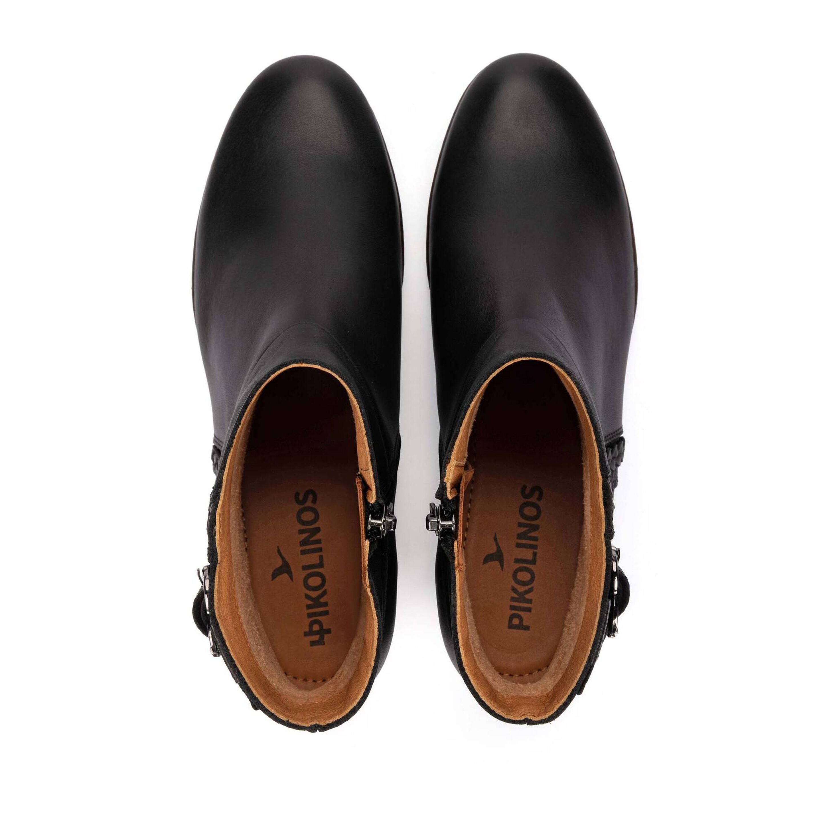 A pair of black leather ankle boots shown from a top-down view on a white background, featuring side zippers and a tan interior with the brand name 'PIKOLINOS' printed on the insole.