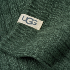Close-up of a dark green ribbed knit fabric with a small beige woven UGG label stitched on the side.