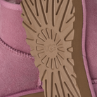 Close-up of the sole of a pink UGG boot, showing the tan rubber tread with the embossed UGG logo and a pink suede upper.