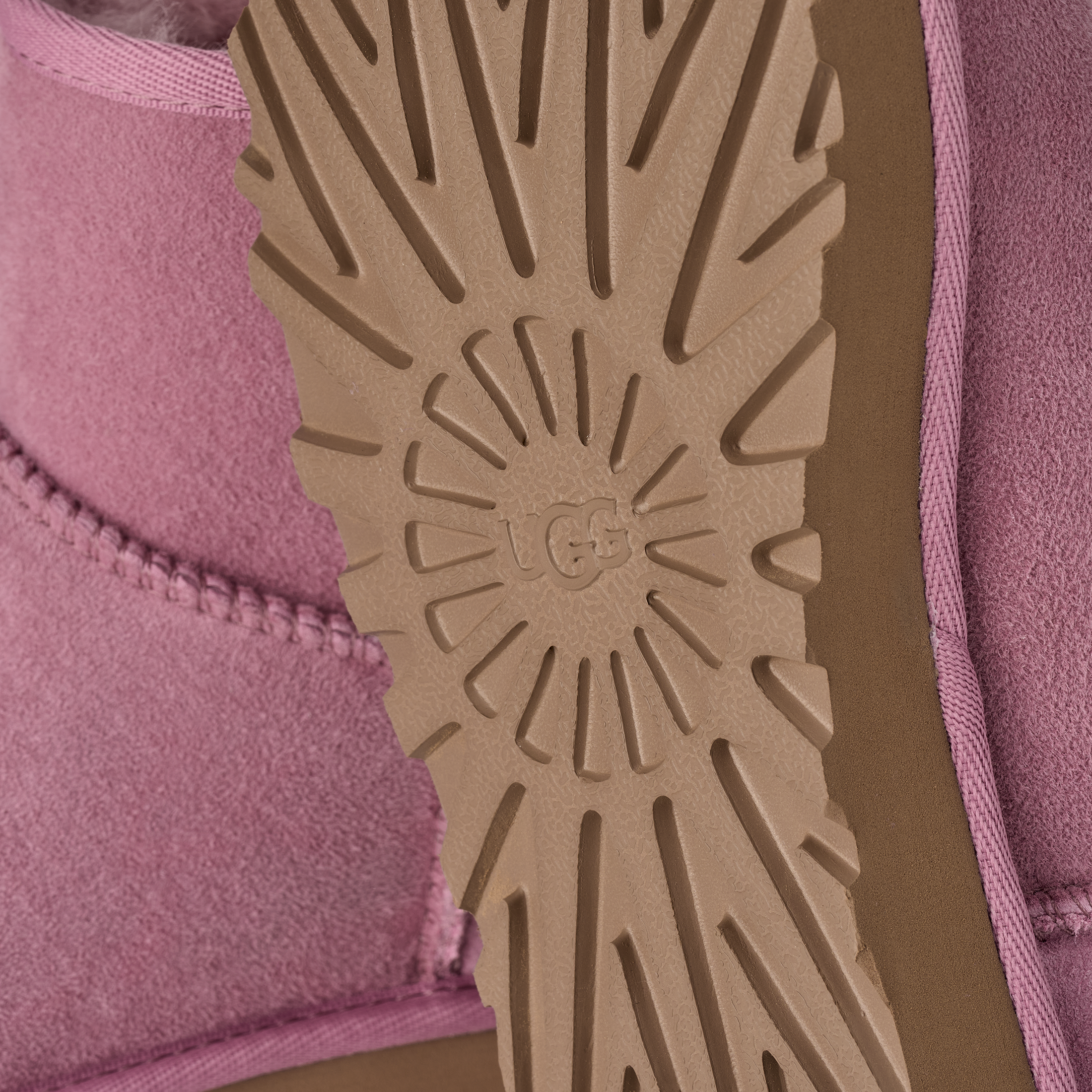 Close-up of the sole of a pink UGG boot, showing the tan rubber tread with the embossed UGG logo and a pink suede upper.