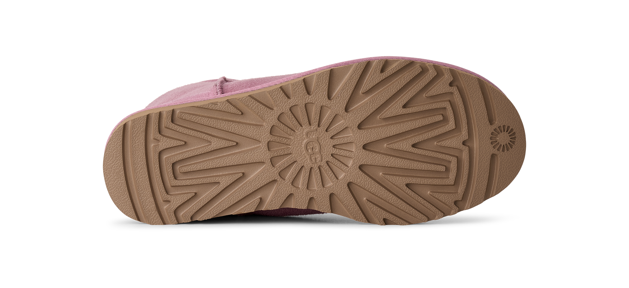 The bottom sole of a pink shoe, showing a textured brown rubber tread with a circular sunburst pattern and a small UGG logo embossed on the heel.