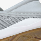 Close-up of a gray shoe with white sole and brown sole tread, featuring the Olukai brand.