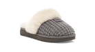 A single UGG slip-on slipper shown from a three-quarter angle on a white background. The slipper features a gray textured knit upper, a soft cream-colored shearling lining, and a dark brown sole.