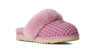 A pink knit slipper with fluffy pink faux-fur trim and a beige sole, shown from a side profile on a white background.