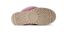 The bottom sole of a pink fuzzy slipper, showing a beige treaded rubber outsole with a circular UGG logo embossed in the center, photographed on a white background.