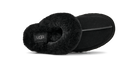 A black UGG slipper shown from a side profile view, featuring a soft black faux-shearling collar and a black suede-like body, with a small black UGG logo patch on the inside.