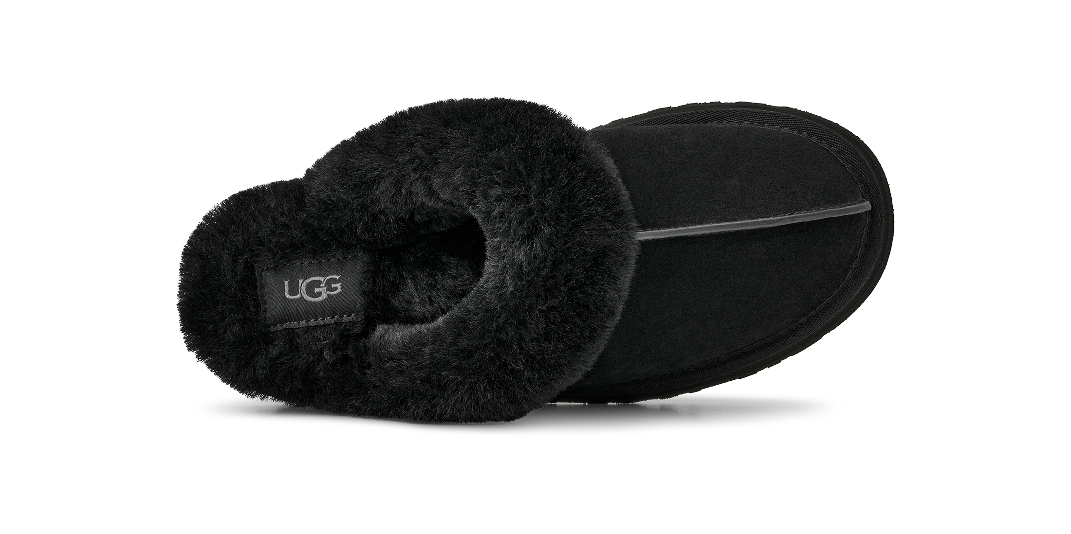 A black UGG slipper shown from a side profile view, featuring a soft black faux-shearling collar and a black suede-like body, with a small black UGG logo patch on the inside.