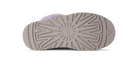 The sole of a UGG slipper in a taupe-brown color, showing the tread pattern and the embossed UGG logo in the center, with a light lavender fuzzy lining visible at the top edge.