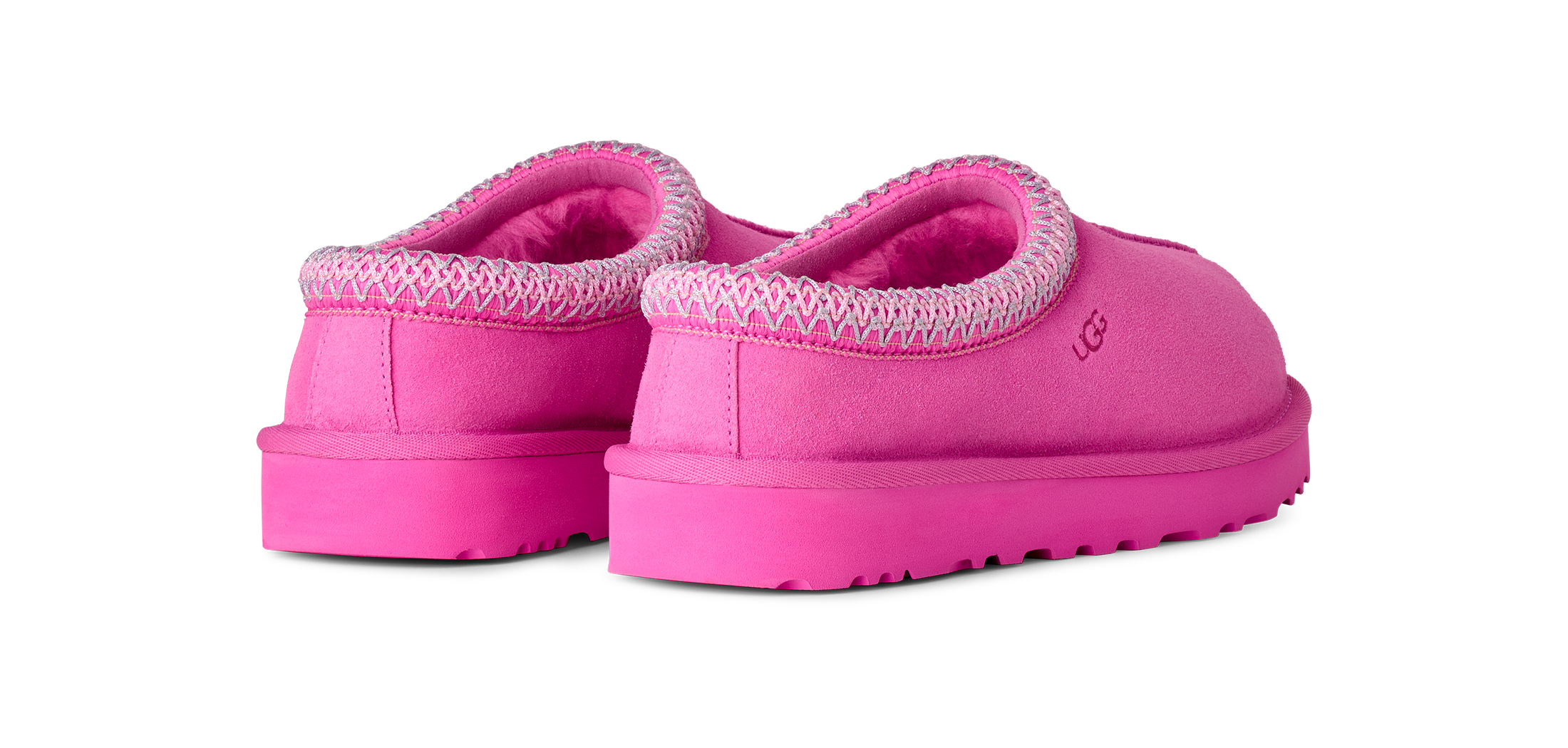 A pair of UGG slip-on slippers in a vibrant pink color, featuring a textured knit trim around the collar and a plush pink interior, shown from a three-quarters angle on a white background.