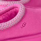 Close-up of a bright pink UGG slipper showing the suede-like exterior, fuzzy pink interior lining, and decorative zigzag trim around the opening.