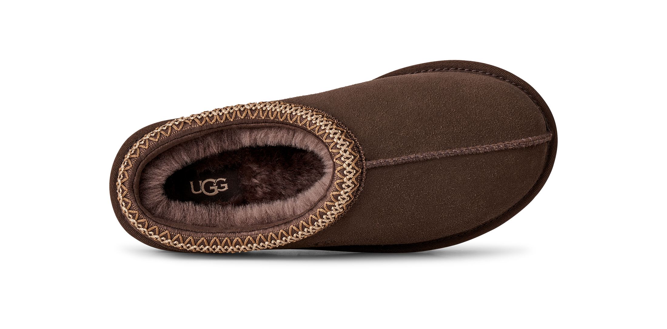 A single brown UGG slipper shown from a side profile view against a white background, featuring a suede-like finish, a decorative braided trim, and a plush brown interior with the UGG logo visible.