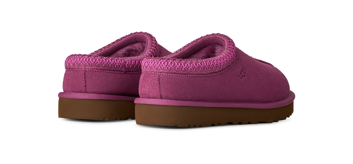 A pair of UGG slip-on slippers in a vibrant magenta pink suede and sherpa fabric, featuring a brown gum sole, shown against a plain white background.
