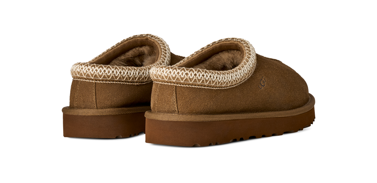 A pair of brown suede slip-on slippers with a textured cream knit trim around the collar and a plush brown lining, shown from a three-quarters angle on a white background.