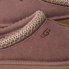 Close-up of a UGG slippers with brown suede and decorative stitching.