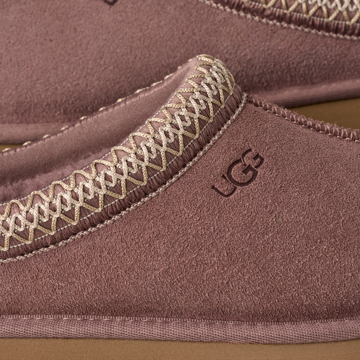 Close-up of a UGG slippers with brown suede and decorative stitching.